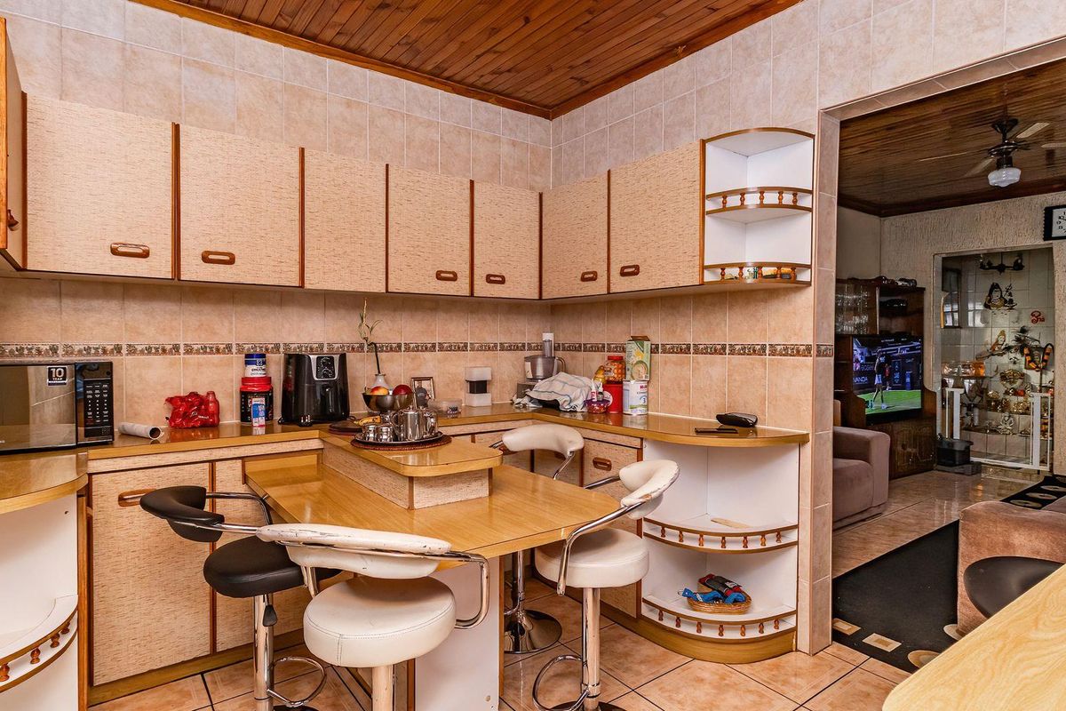 A functional kitchen featuring laminate cabinetry, tiled splashbacks, and a built-in breakfast bar, with an open-plan flow into the adjacent living area.