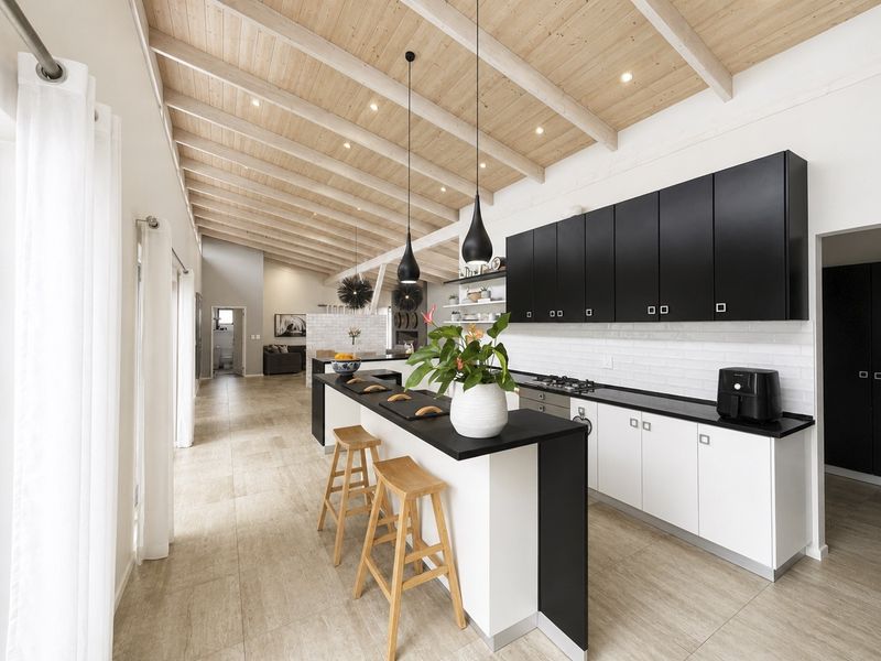 Modern open-plan kitchen featuring a striking black and white cabinetry design, exposed timber beam ceiling, and a functional island with breakfast bar seating.