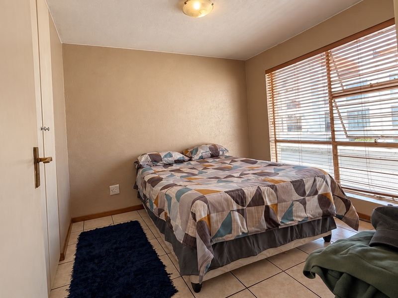 A functional bedroom featuring tiled flooring, neutral wall finishes, and large windows fitted with venetian blinds for natural light control.