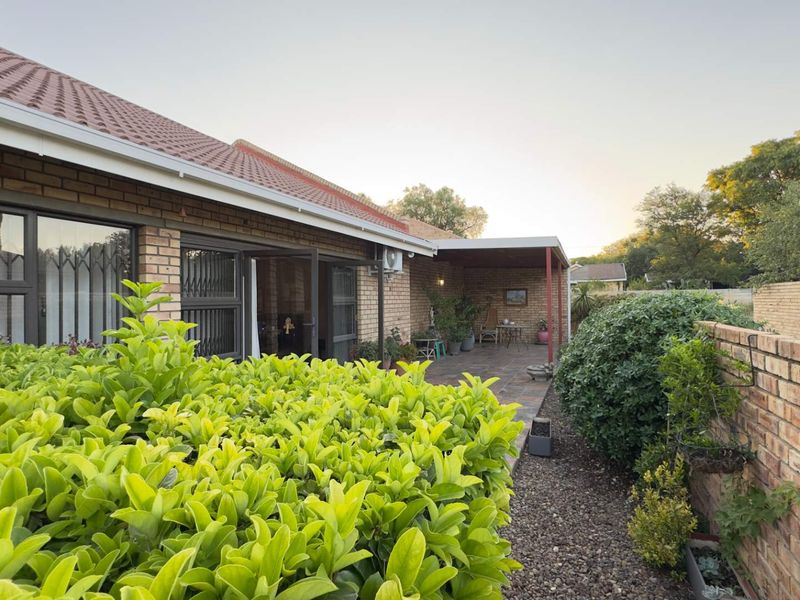 A rear view of the house featuring a paved patio area, brick exterior walls, tiled roof, and established garden landscaping.