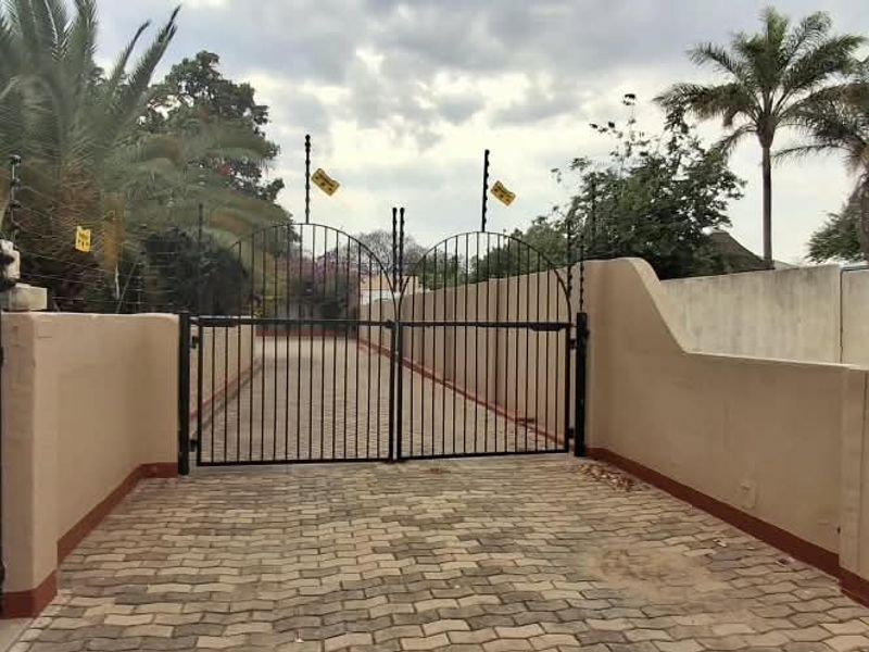 A secure entrance featuring a paved driveway, perimeter walling, and metal security gates equipped with electric fencing.
