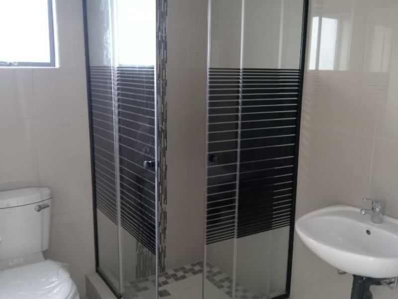A clean, modern bathroom featuring a corner shower enclosure with black frame detailing, a wall-mounted basin, and a standard toilet.