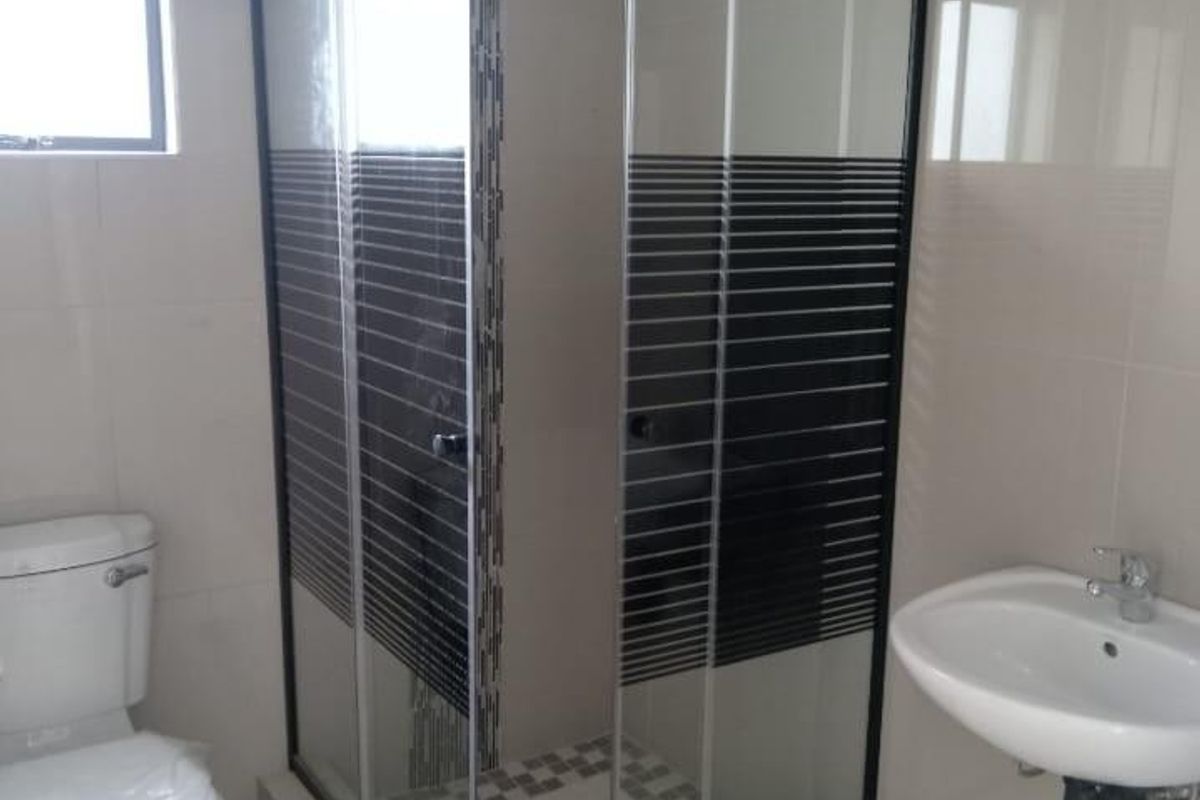 A clean, modern bathroom featuring a corner shower enclosure with black frame detailing, a wall-mounted basin, and a standard toilet.
