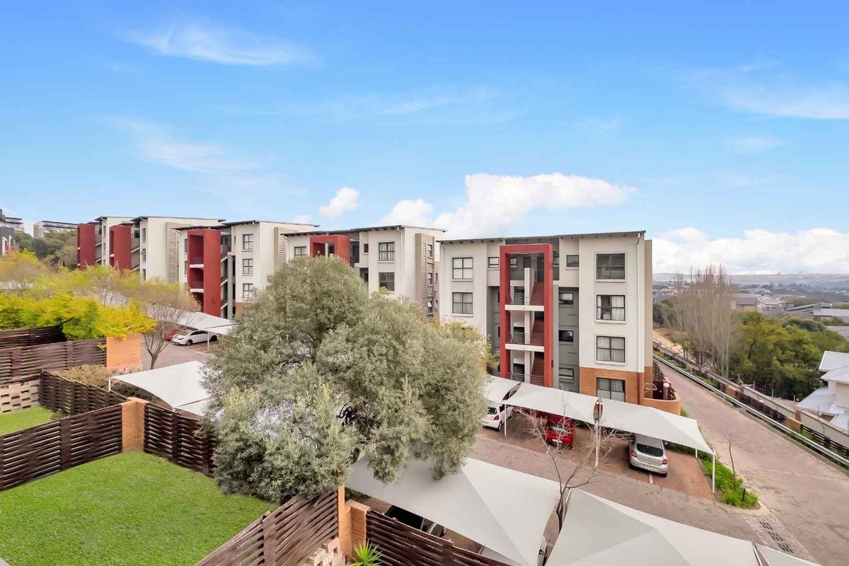 Elevated view of the apartment complex featuring covered parking bays, landscaped garden areas, and secure perimeter fencing.