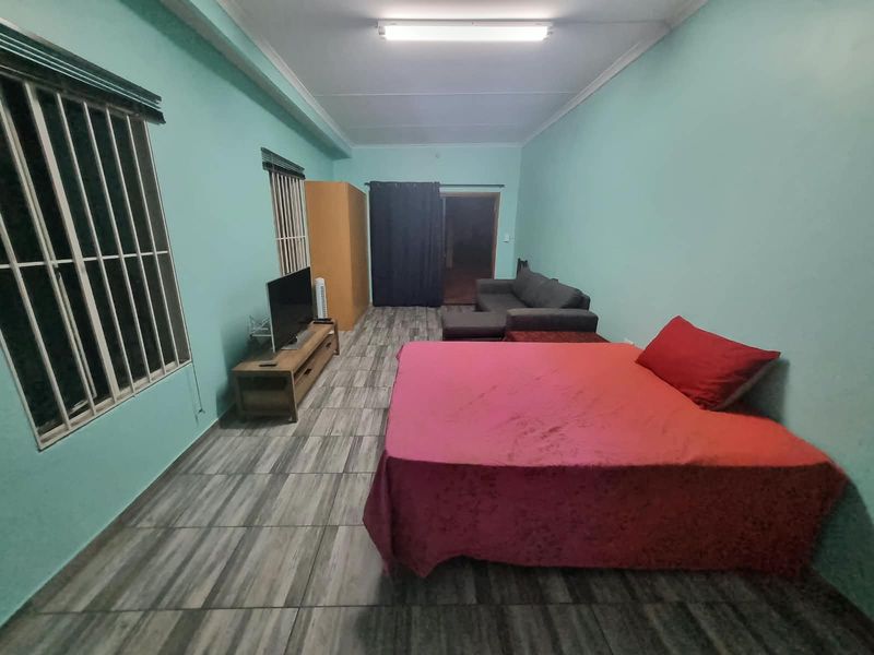 A spacious bedroom featuring tiled flooring, security bars on the windows, and a functional layout suitable for various furniture arrangements.