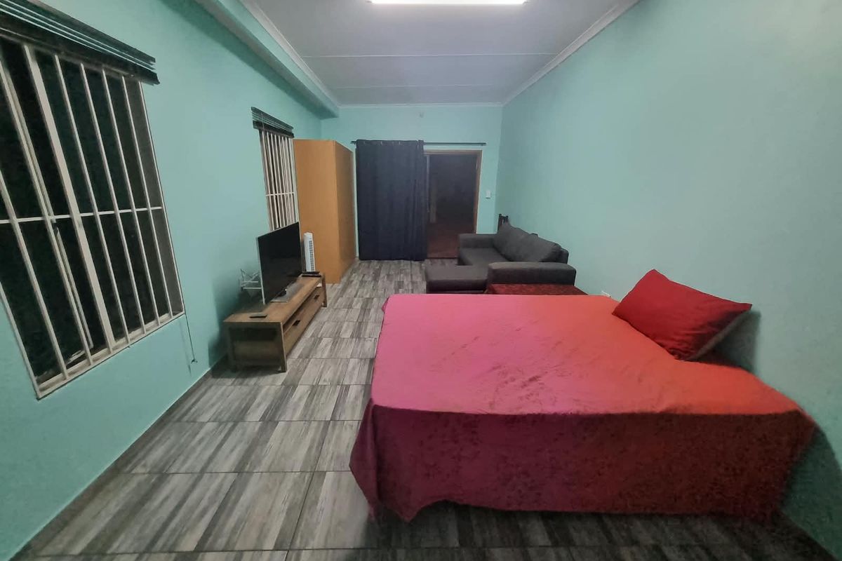 A spacious bedroom featuring tiled flooring, security bars on the windows, and a functional layout suitable for various furniture arrangements.