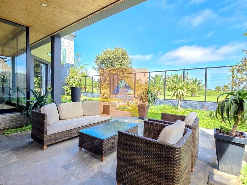 A covered patio area featuring stone flooring, a timber-clad ceiling with recessed lighting, and a glass balustrade overlooking the garden.