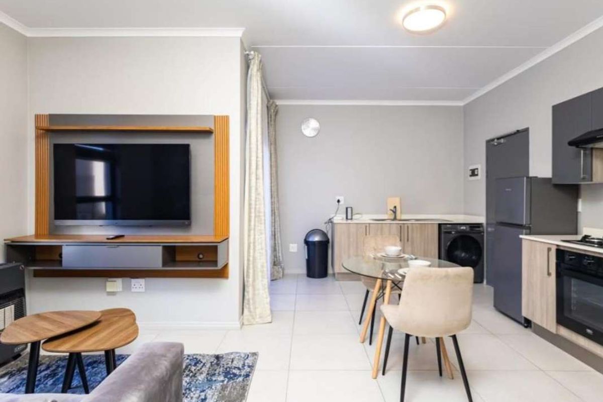 Modern open-plan living area featuring a sleek kitchen with built-in appliances and a dedicated media wall, finished with neutral tones and tiled flooring.
