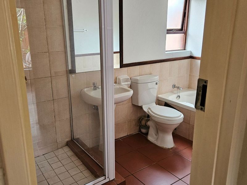 A functional bathroom featuring a shower enclosure, pedestal basin, toilet, and built-in bathtub with neutral ceramic tiling throughout.