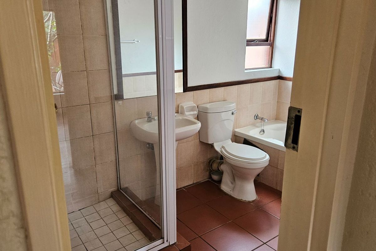 A functional bathroom featuring a shower enclosure, pedestal basin, toilet, and built-in bathtub with neutral ceramic tiling throughout.