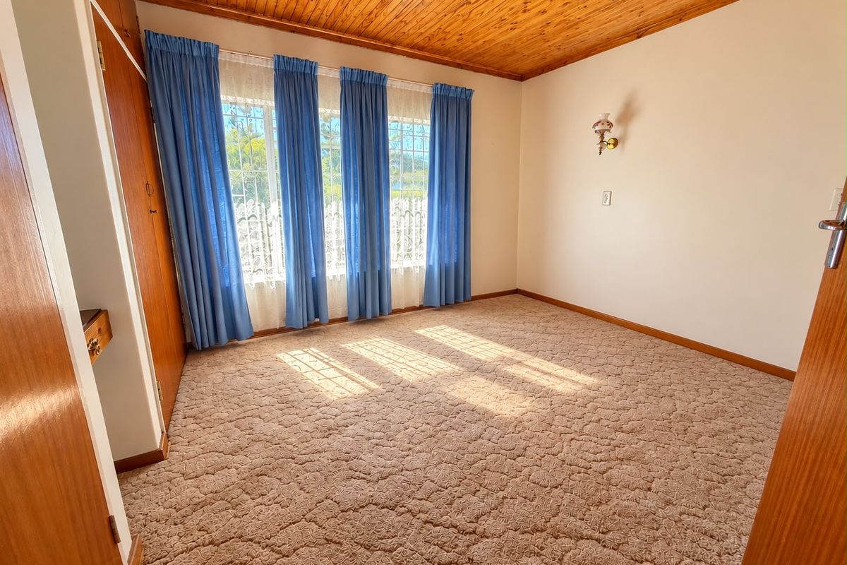 A spacious, empty bedroom featuring a warm timber tongue and groove ceiling, built-in cupboards, and large windows with security bars.