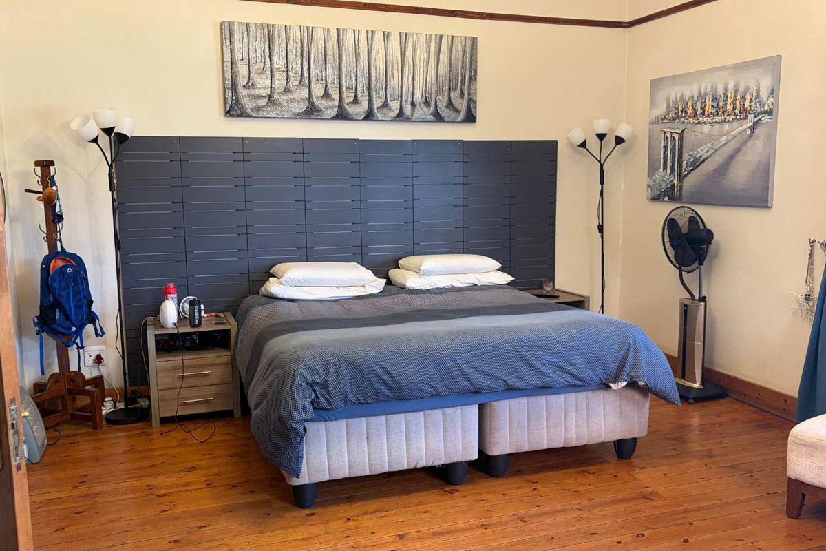 A spacious bedroom featuring polished timber flooring and a decorative dark feature wall panel behind the bed area.