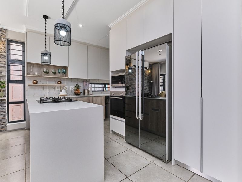 Modern kitchen featuring a central island, stone countertops, built-in appliances, and a stylish stone-clad feature wall with contemporary pendant lighting.