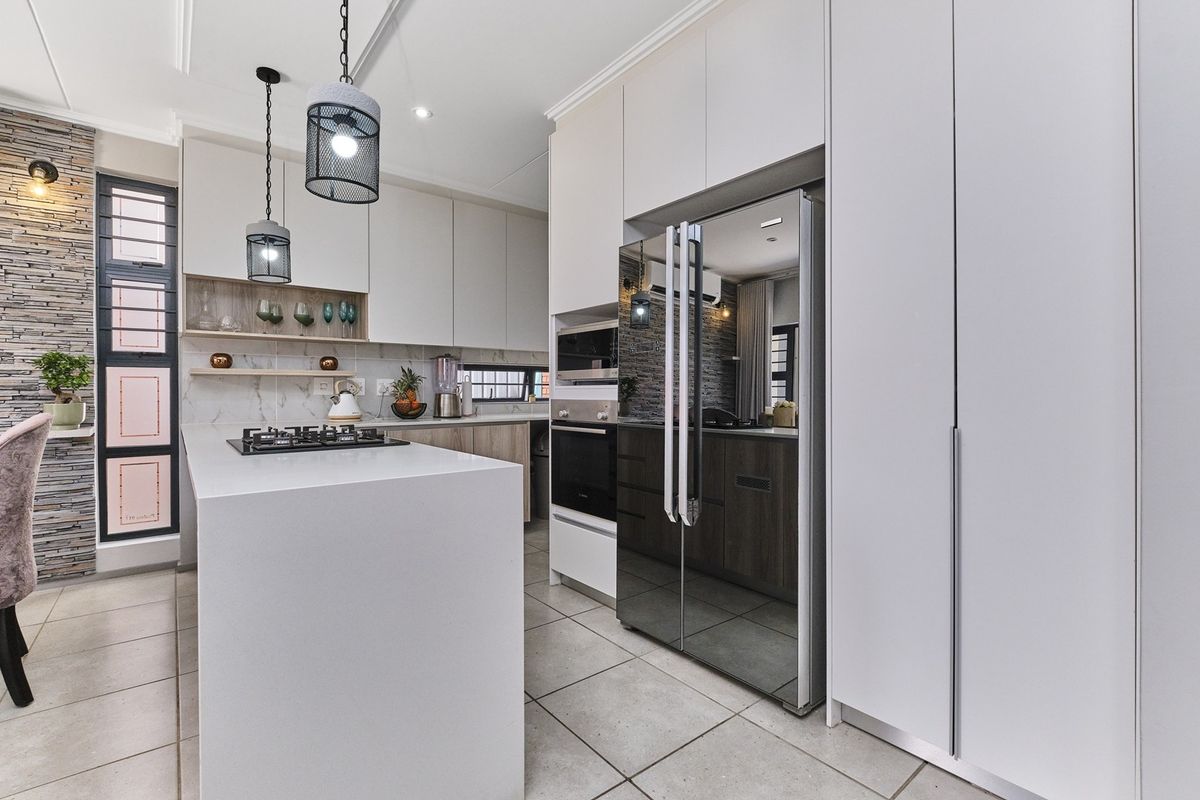 Modern kitchen featuring a central island, stone countertops, built-in appliances, and a stylish stone-clad feature wall with contemporary pendant lighting.