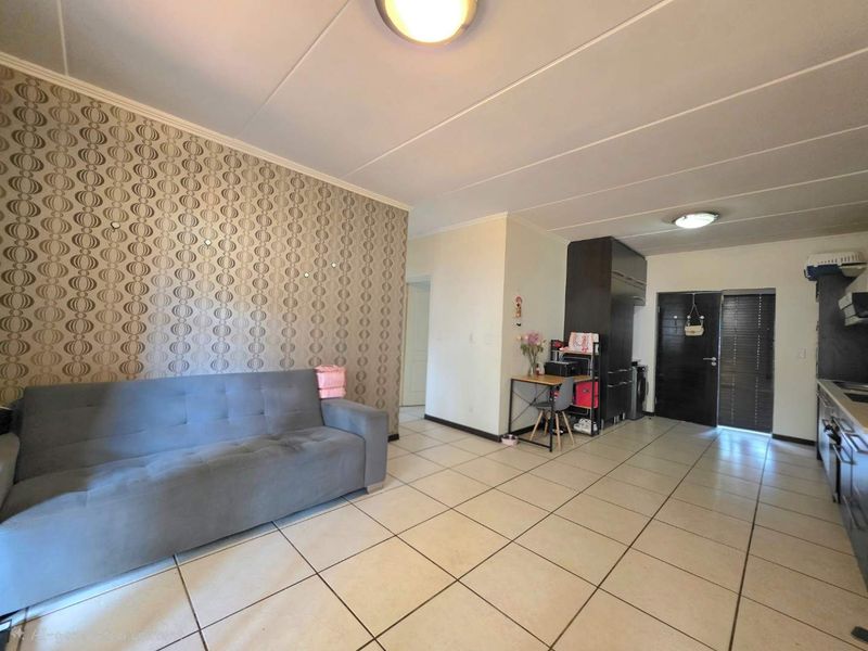 Open-plan living area featuring tiled flooring, a feature wallpaper wall, and a compact kitchen with built-in cabinetry and appliances.
