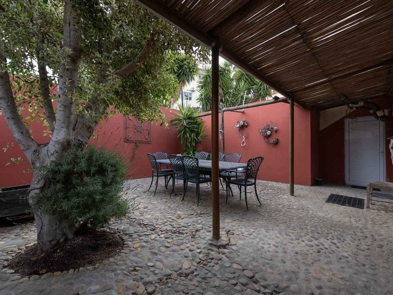A private outdoor patio area featuring cobblestone flooring, a bamboo-covered pergola, and enclosed masonry walls, providing a shaded space for outdoor dining.