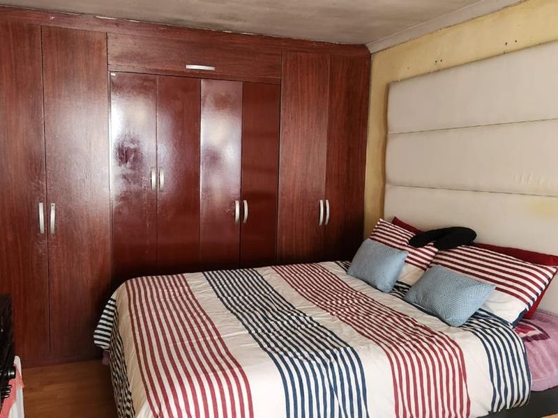 Bedroom featuring extensive built-in wooden cupboards, laminate flooring, and a large upholstered headboard. The room requires cosmetic updates to the walls and ceiling.
