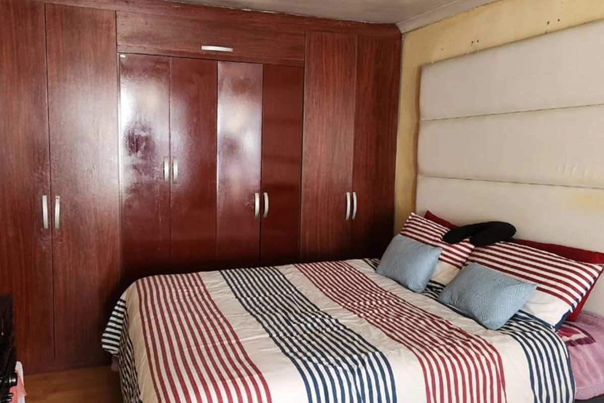 Bedroom featuring extensive built-in wooden cupboards, laminate flooring, and a large upholstered headboard. The room requires cosmetic updates to the walls and ceiling.