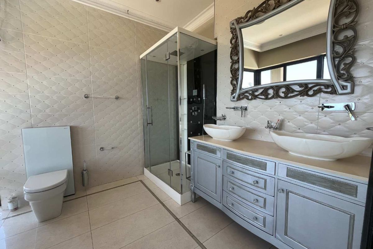 Modern bathroom featuring a double vanity with vessel sinks, a glass-enclosed shower, and wall-mounted toilet with a sleek, tiled finish.