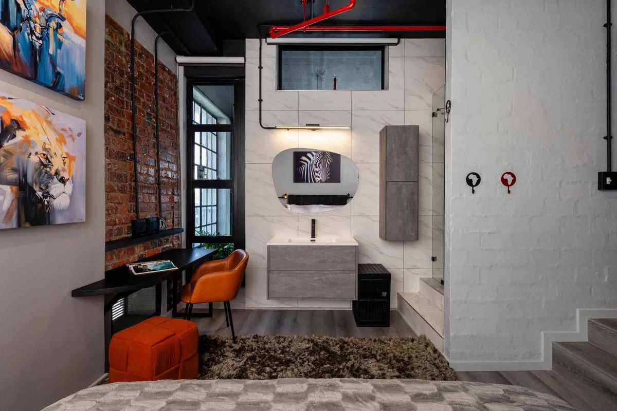 Modern industrial-style bedroom featuring an exposed brick wall, integrated desk space, and an en-suite bathroom area with contemporary vanity and glass shower.