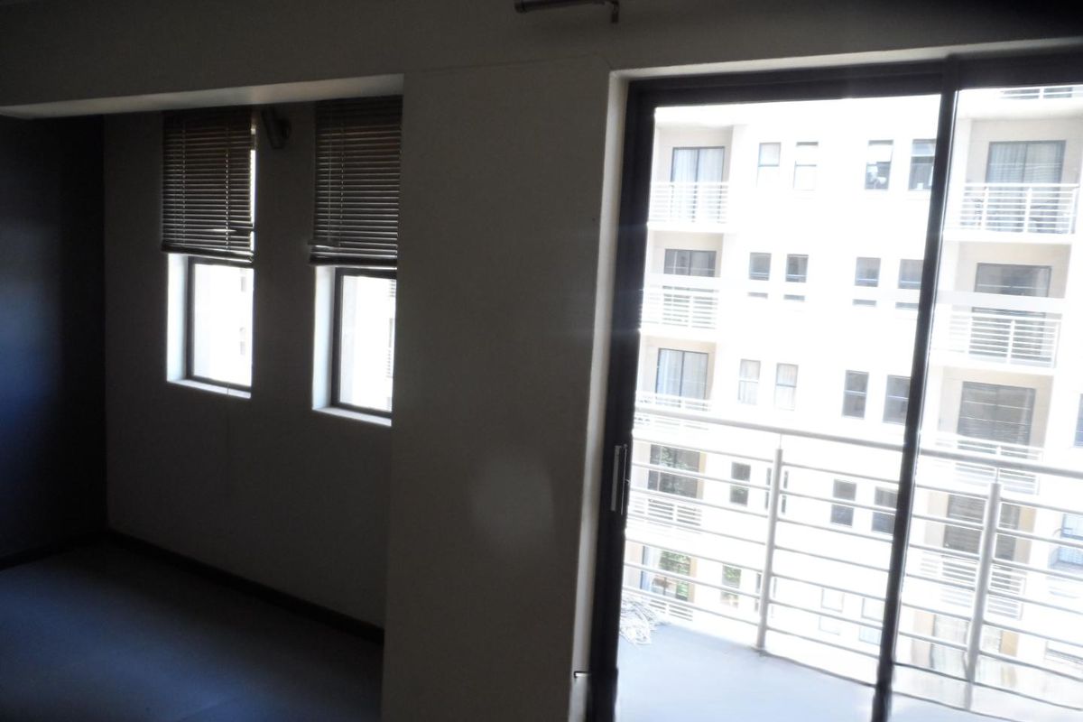 An empty living area featuring sliding glass doors leading to a balcony and fitted venetian blinds on the windows.