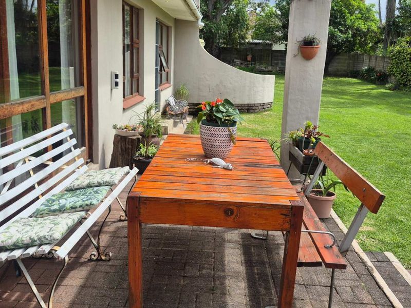 A covered paved patio area featuring timber-framed sliding doors, overlooking a spacious private garden.