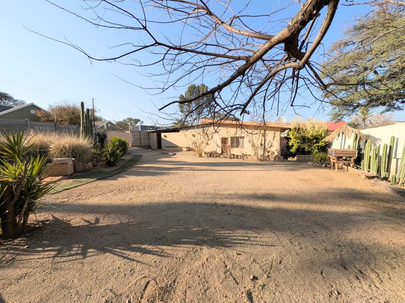 A spacious rear yard featuring a gravel surface, boundary walls, and established garden beds, offering potential for landscaping or outdoor development.