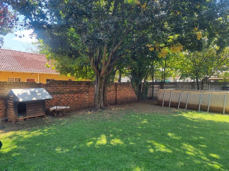 A spacious backyard featuring a large lawn, mature trees, and a brick boundary wall, providing a private outdoor area.