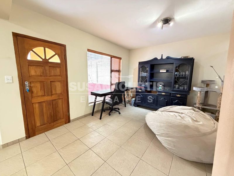 A living area featuring tiled flooring, a solid timber front door, and a large window with fitted blinds.
