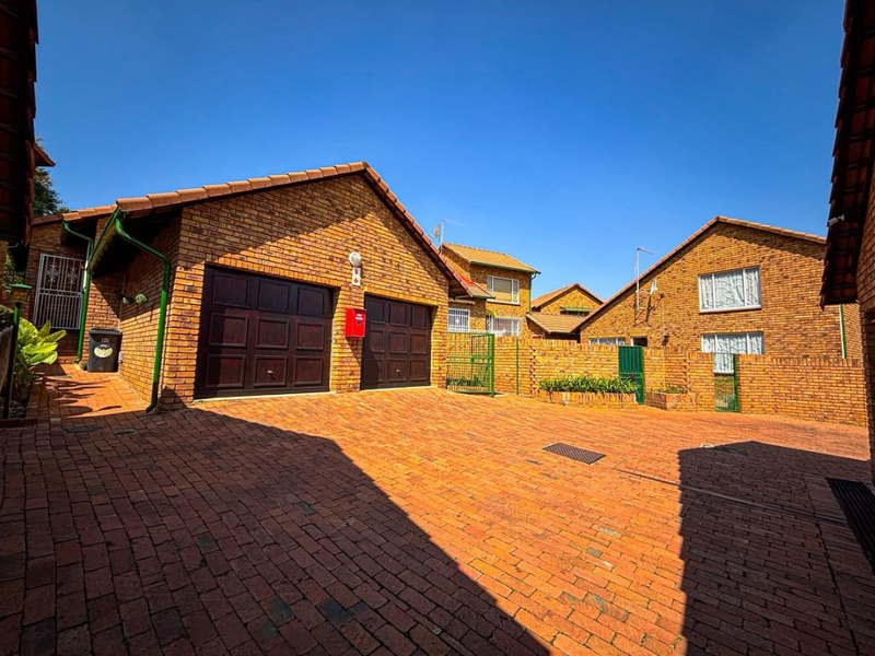 A well-maintained townhouse exterior featuring a face brick facade, double garage, and a spacious paved driveway within a secure complex setting.