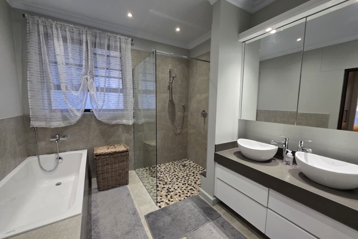 Modern bathroom featuring a double vanity with vessel sinks, a frameless glass walk-in shower with pebble flooring, and a separate bathtub.