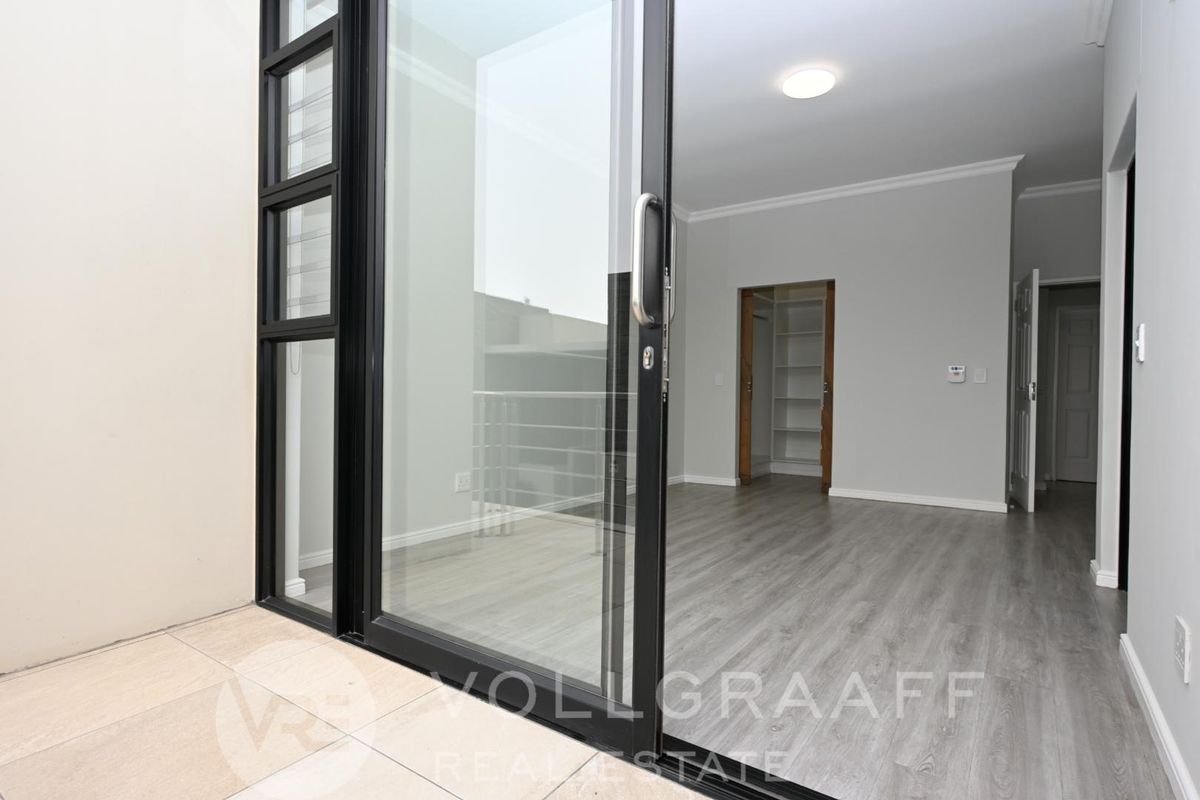 A bright interior view looking from a tiled balcony through large sliding glass doors into a modern room with light wood-look flooring.