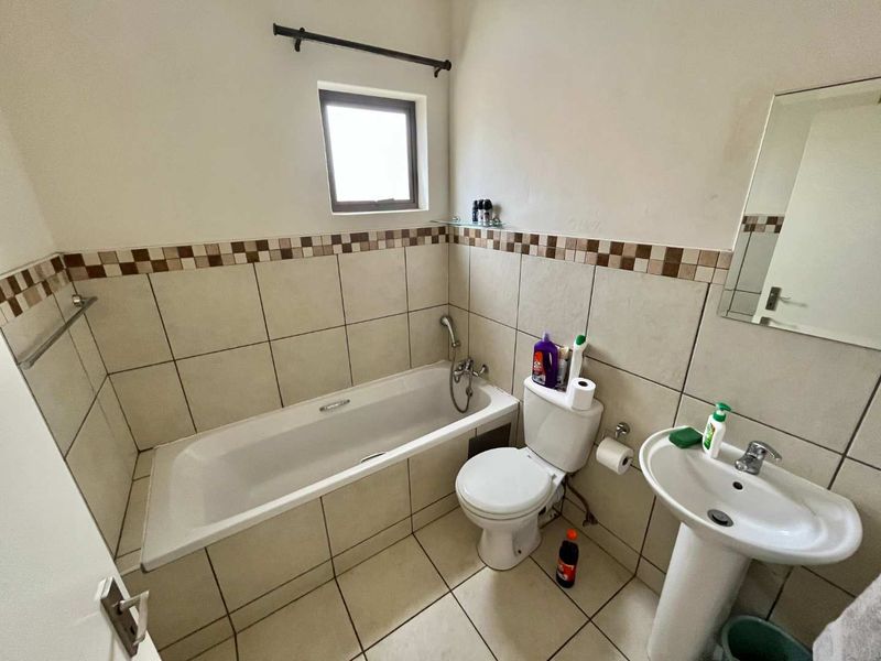 A functional bathroom featuring a bathtub, pedestal basin, and toilet with neutral wall and floor tiling.