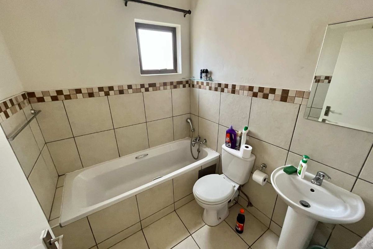 A functional bathroom featuring a bathtub, pedestal basin, and toilet with neutral wall and floor tiling.