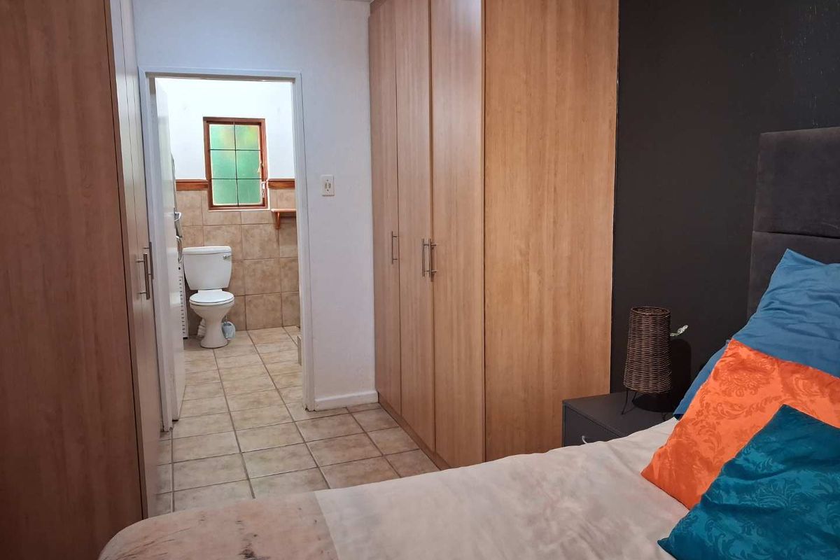 A bedroom featuring built-in wooden cupboards and an en-suite bathroom with tiled flooring and a window.