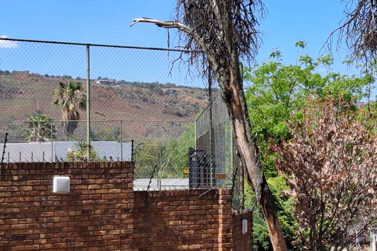 View of a brick boundary wall with security fencing and surrounding vegetation, set against a hillside backdrop.