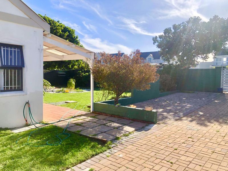 Rear garden area featuring a paved patio, covered outdoor space, and a low retaining wall, providing a functional outdoor living area.