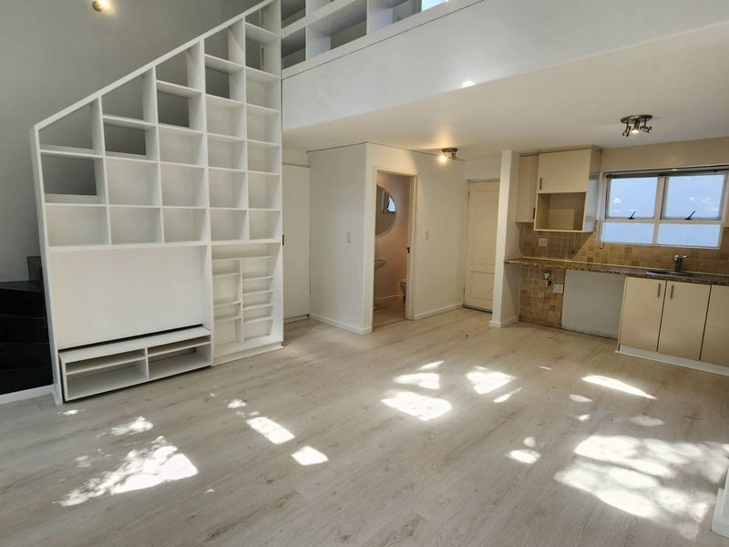 Open-plan living area featuring a mezzanine level, built-in shelving, and a functional kitchen with granite countertops and ample cabinetry.