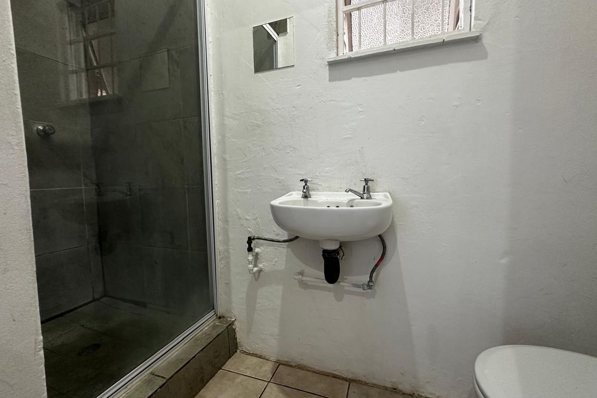 A functional bathroom featuring a glass-enclosed shower, wall-mounted basin with exposed plumbing, and tiled flooring.