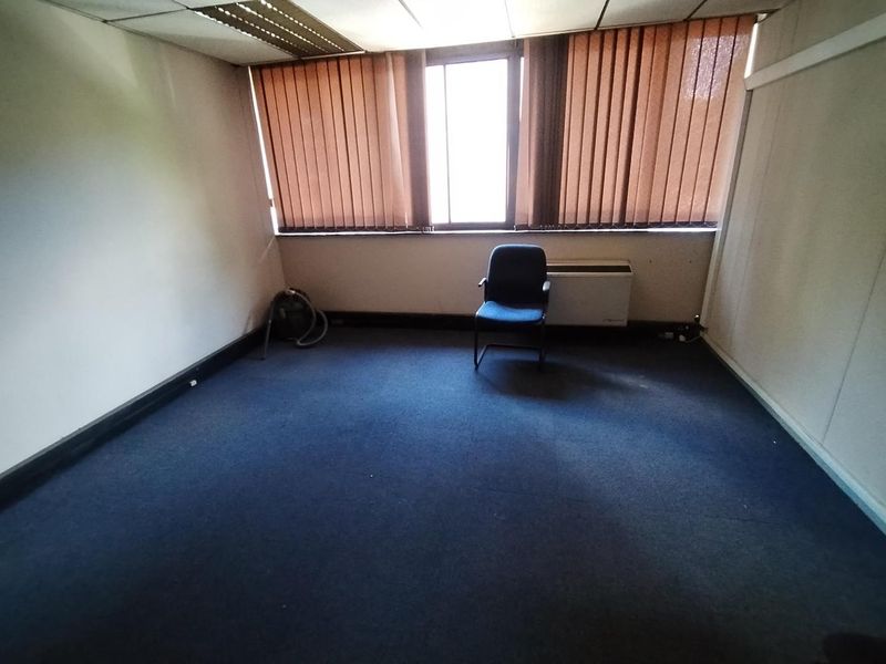 A vacant office space featuring blue carpeting, vertical window blinds, and a wall-mounted HVAC unit.