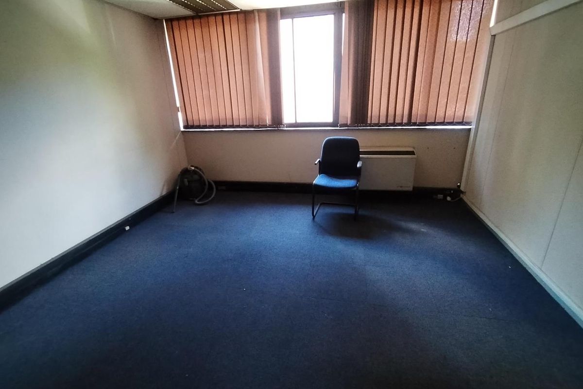 A vacant office space featuring blue carpeting, vertical window blinds, and a wall-mounted HVAC unit.