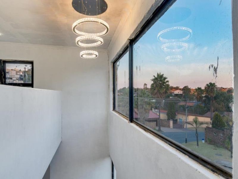 A bright, double-volume living area featuring large picture windows, modern pendant lighting, and a clean, minimalist aesthetic with views of the surrounding neighborhood.