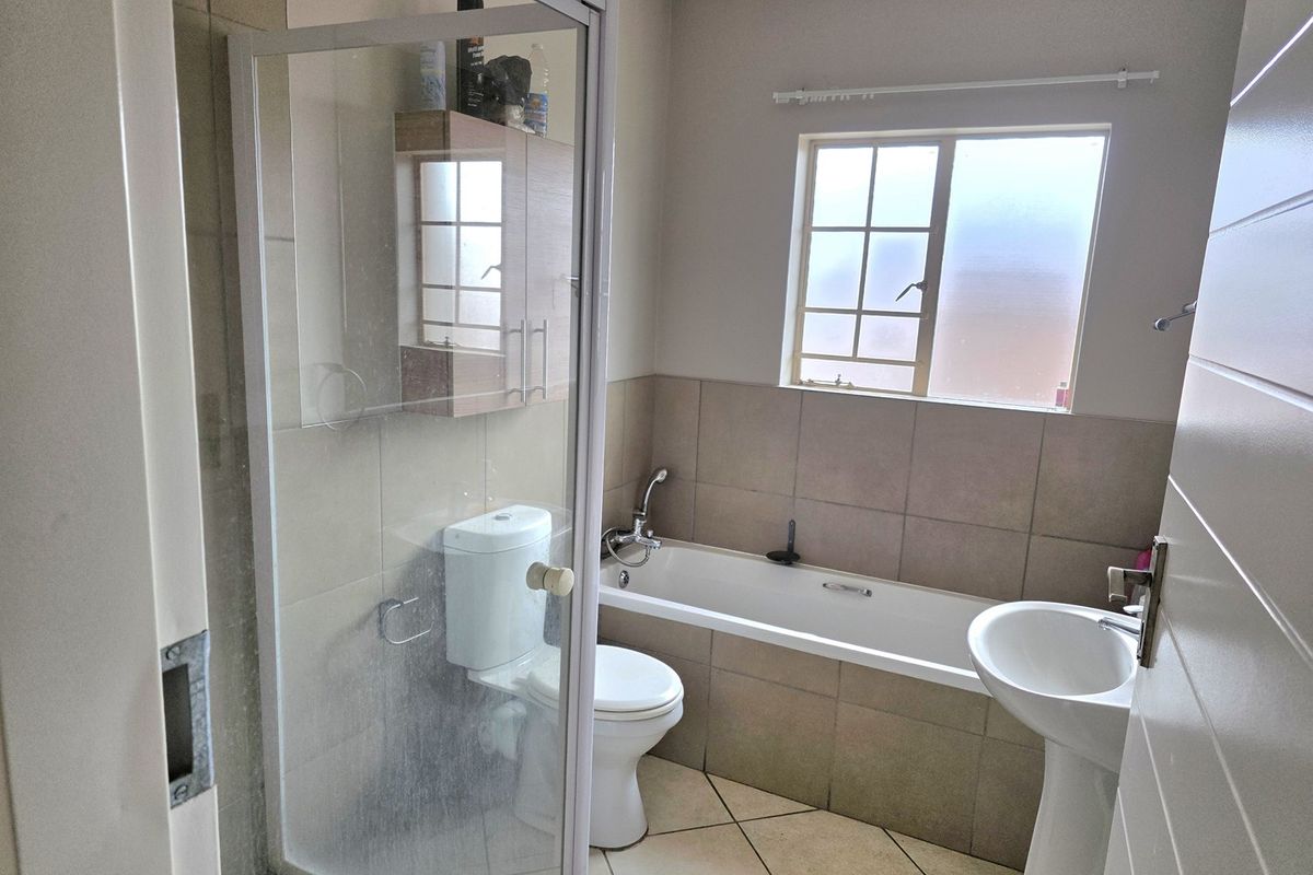A functional bathroom featuring a shower enclosure, bathtub, pedestal basin, and neutral wall and floor tiling with a built-in storage cabinet.