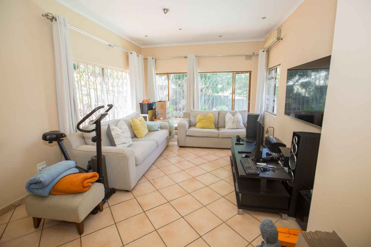 A spacious living room featuring tiled flooring, large windows with security bars, and a wall-mounted air conditioning unit.