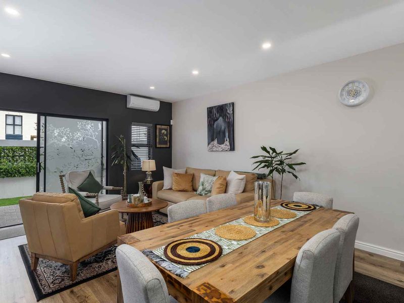 Open-plan living and dining area featuring laminate flooring, recessed downlighting, a split-system air conditioner, and direct access to an outdoor patio space.