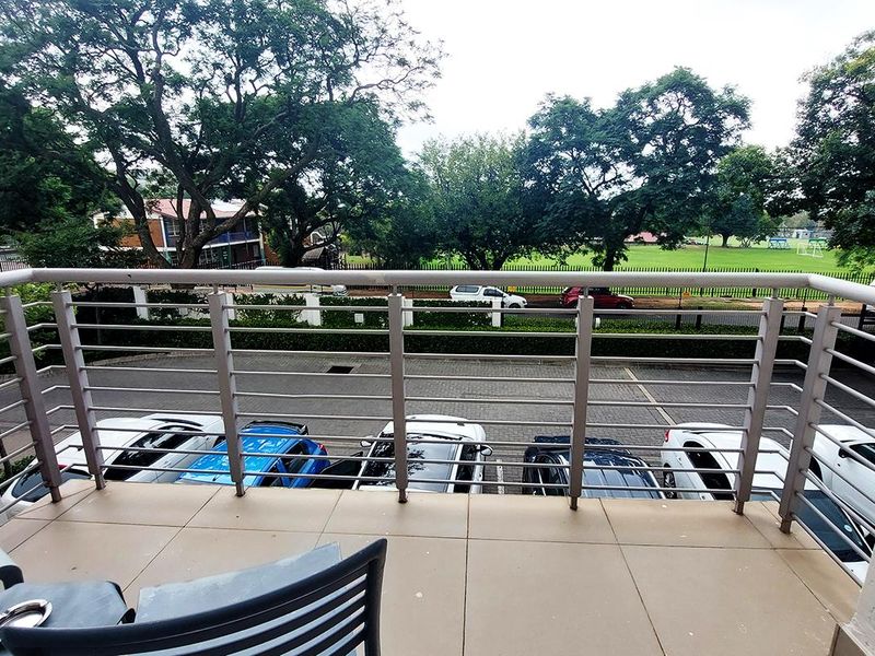 A private balcony featuring tiled flooring and a secure metal balustrade, overlooking the parking area and surrounding greenery.