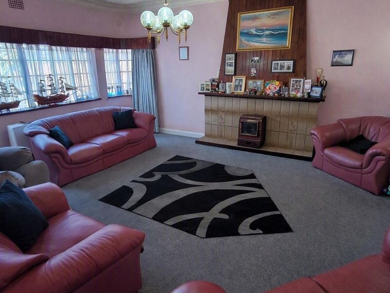A spacious living room featuring a traditional tiled fireplace with a built-in stove, decorative ceiling cornicing, and large windows allowing natural light.