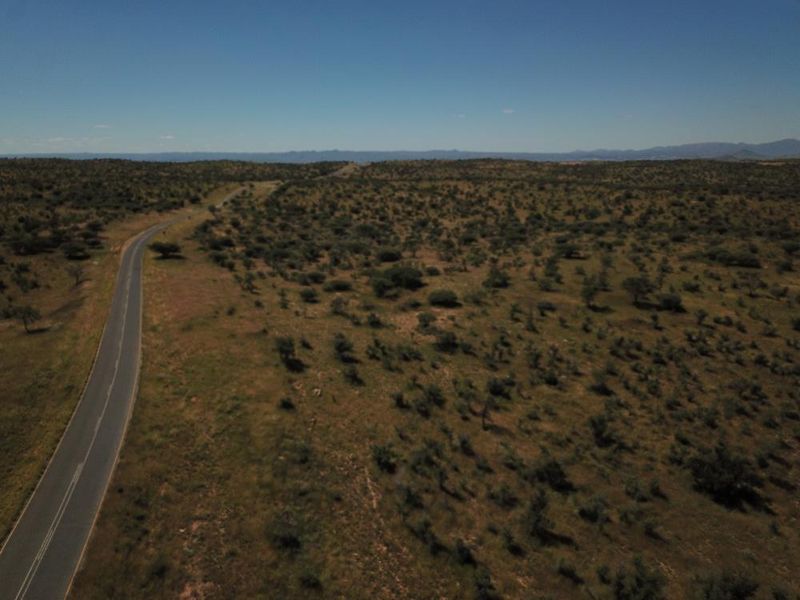 An aerial view of a vast, undeveloped residential land parcel featuring natural vegetation and adjacent road access.