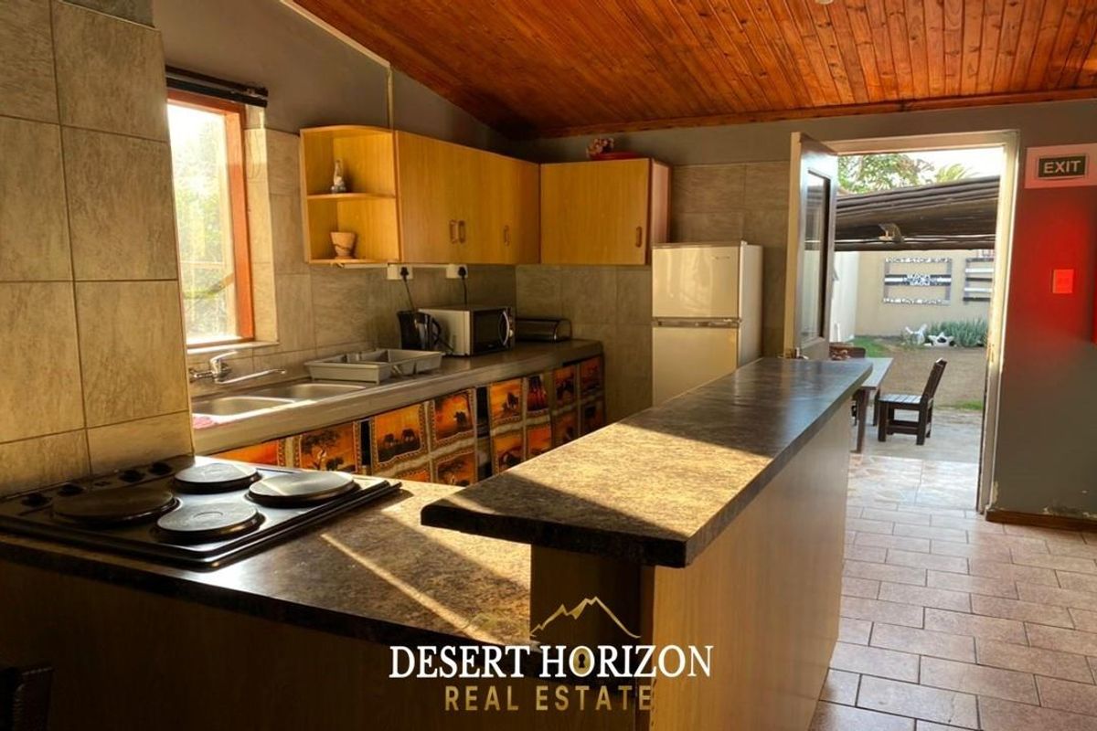 A functional kitchen featuring built-in cabinetry, laminate countertops, an electric hob, and a double sink, with direct access to an outdoor patio area.