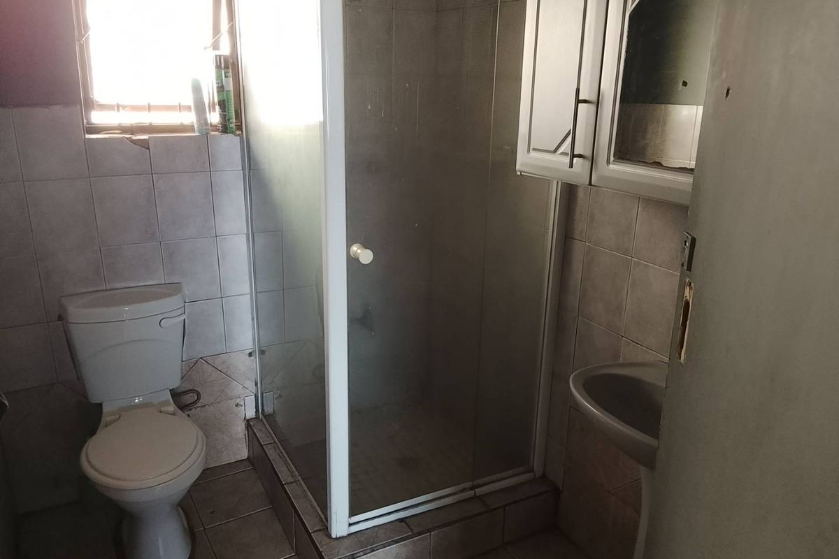 A compact bathroom featuring a shower enclosure, pedestal basin, and toilet, finished with tiled walls and flooring. Requires cosmetic updates.